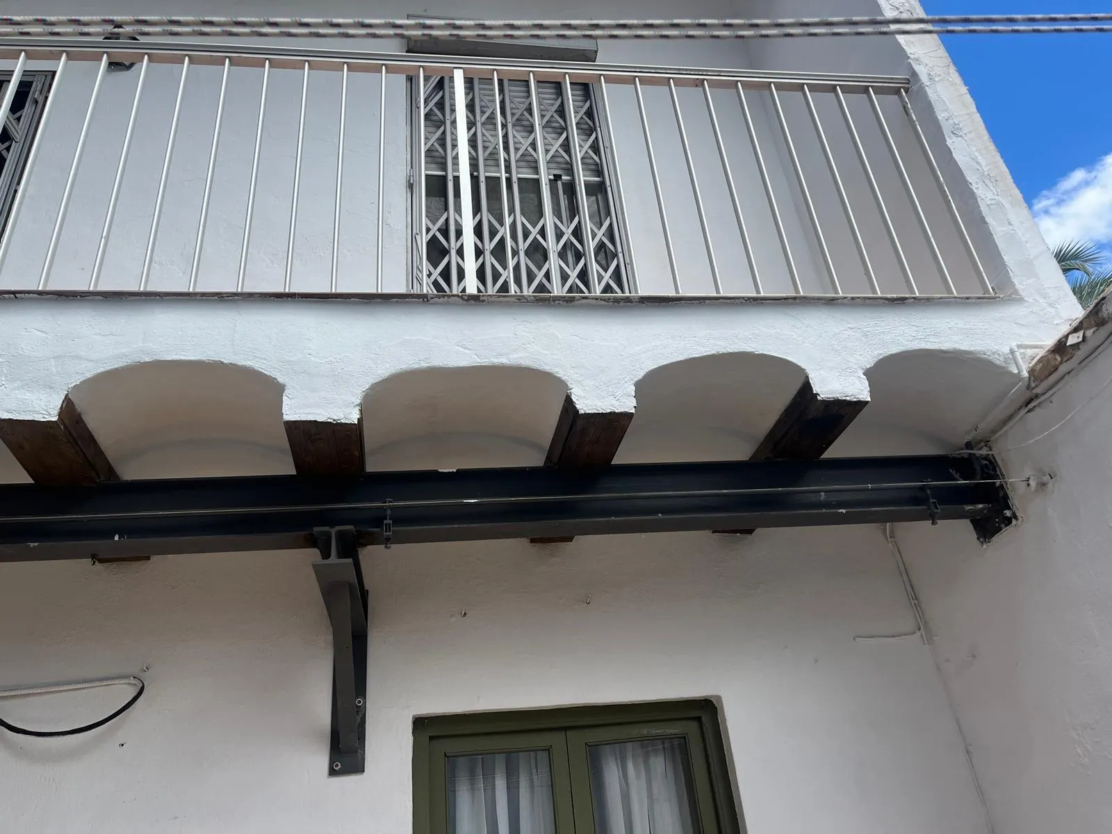 Viga metálica y ménsula de refuerzo bajo un balcón con barandilla blanca