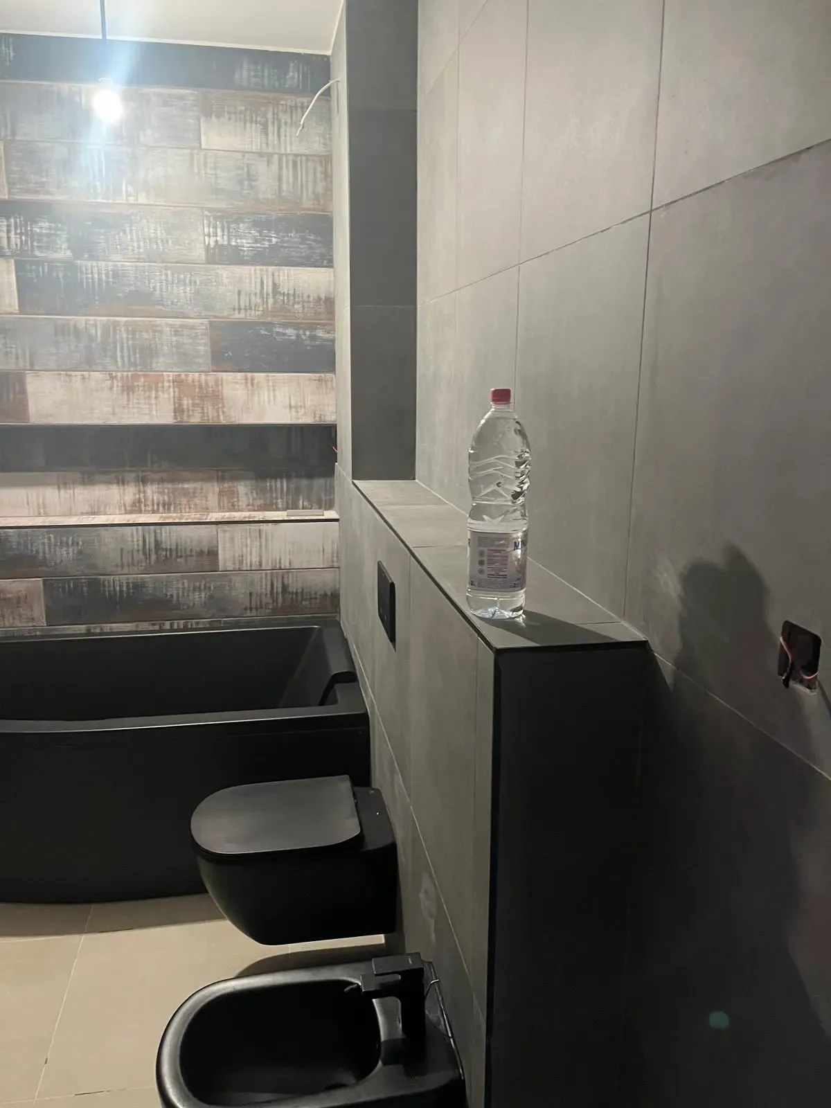 Baño con bañera negra, sanitarios suspendidos en negro mate y revestimiento efecto madera envejecida