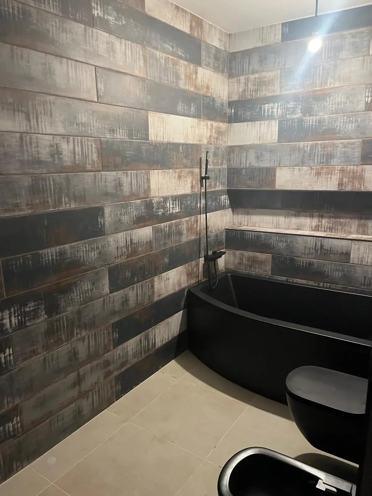 Baño con revestimiento oscuro efecto madera y bañera negra