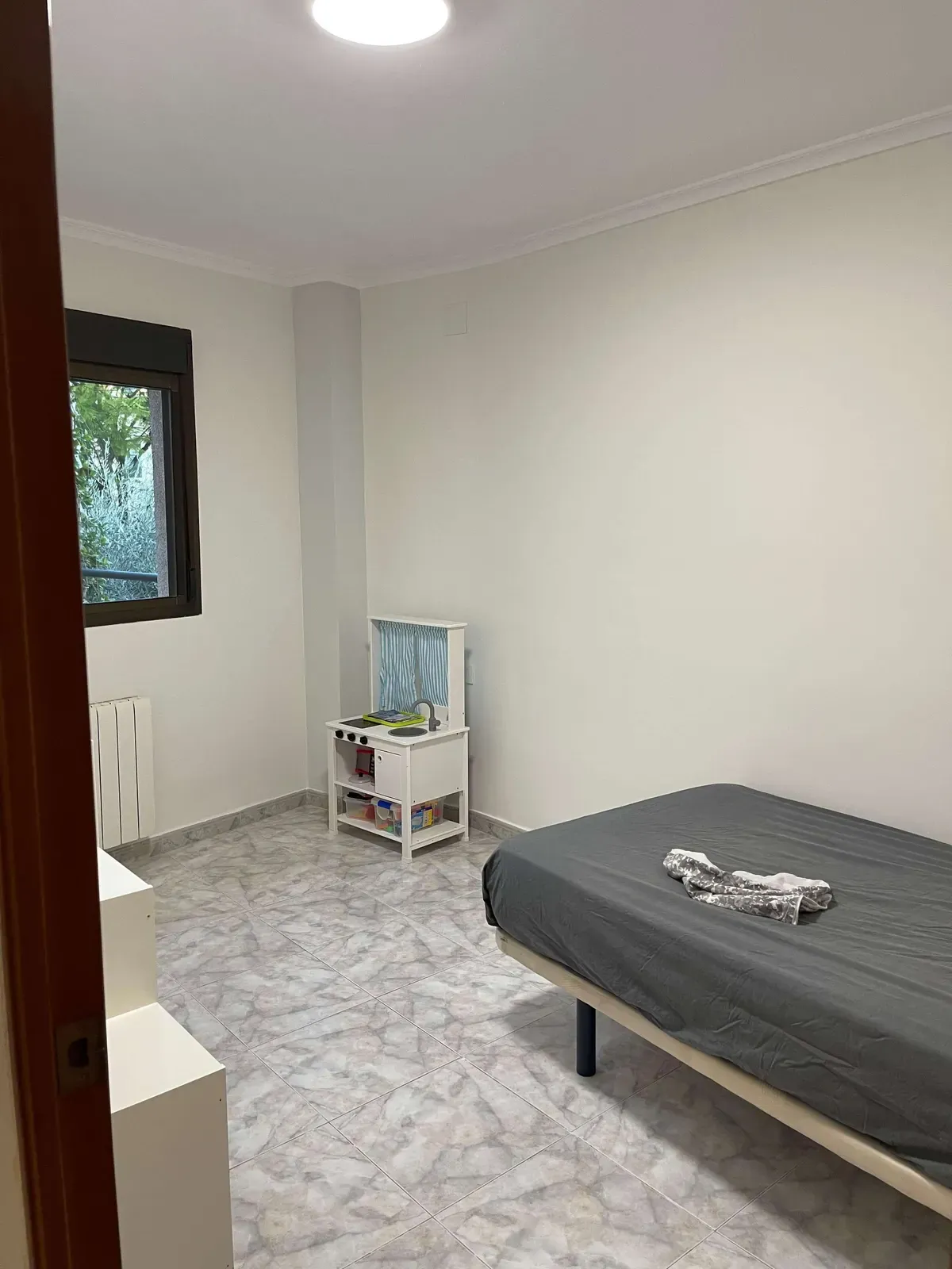 Habitación con paredes blancas, radiador y cama